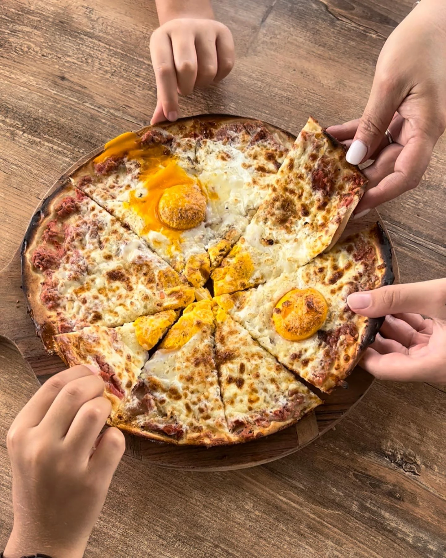 Hands sharing freshly baked meat, cheese and egg manoushe around a wooden table